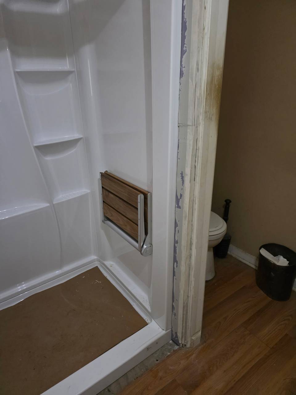 New white shower with a fold-down teak shower seat mounted on the wall