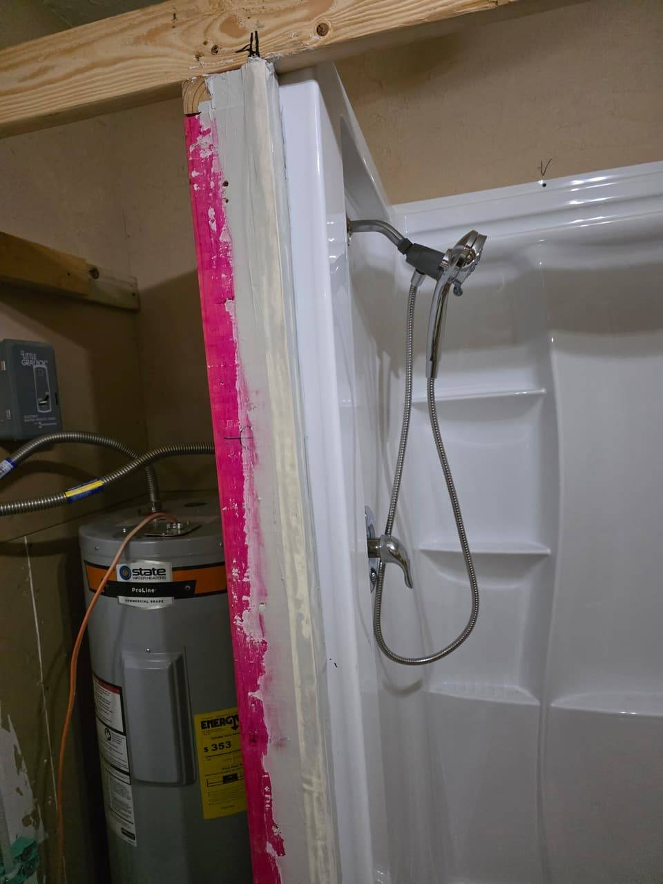 Electric water heater with flexible connections next to a newly installed shower surround