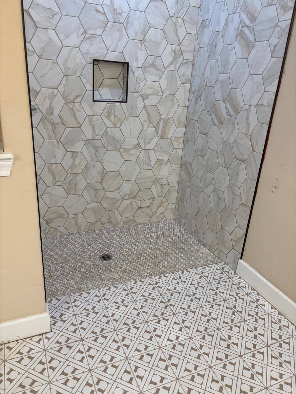 Walk-in shower finished with large hexagon marble-look tile, a recessed niche and a penny-tile floor