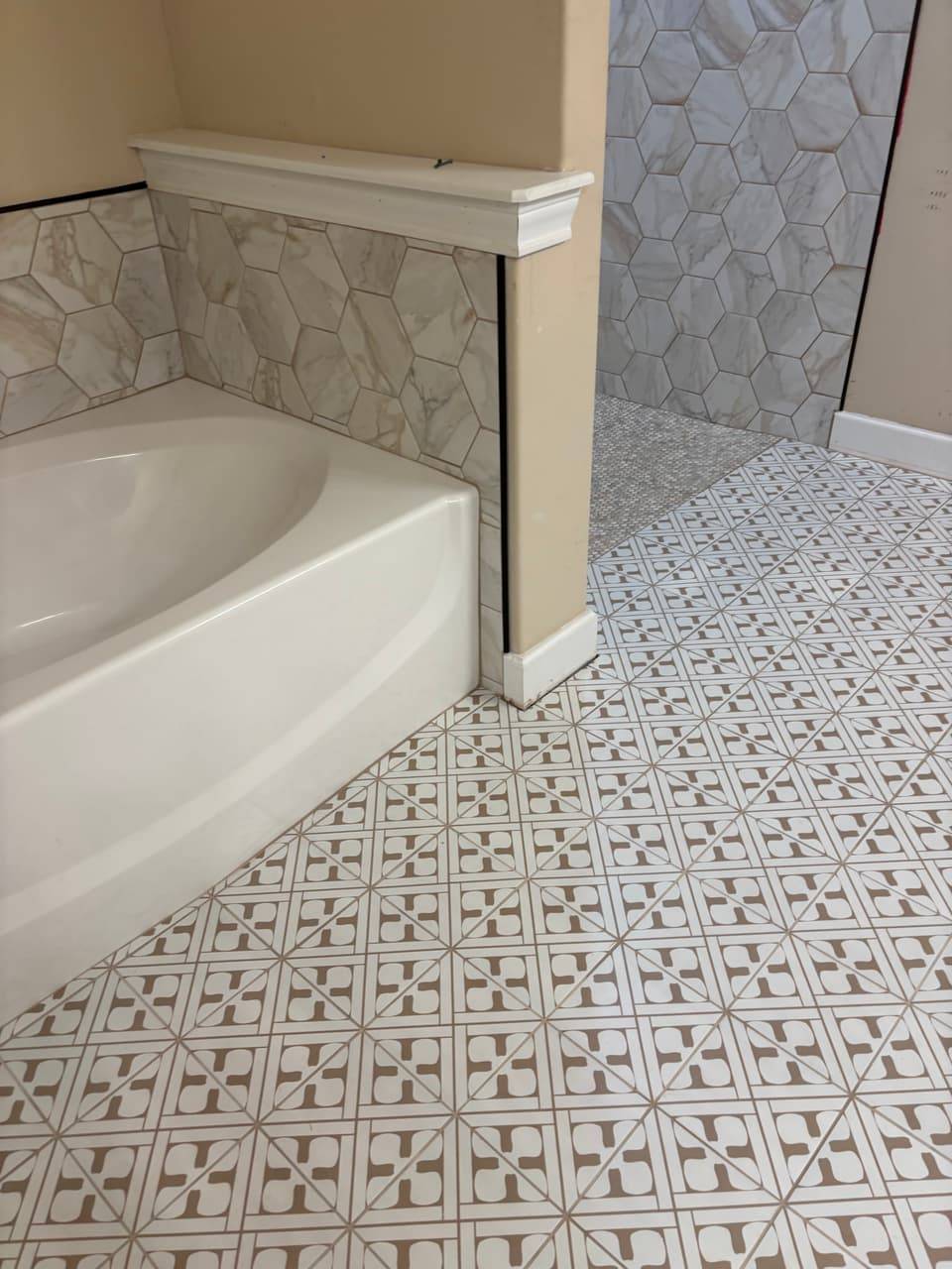 Corner of a soaking tub with a hexagon tile surround and patterned floor tile