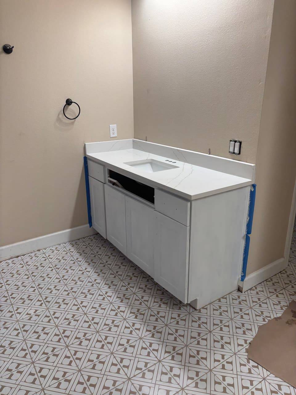 New white shaker vanity with a quartz countertop and undermount sink on a patterned tile floor